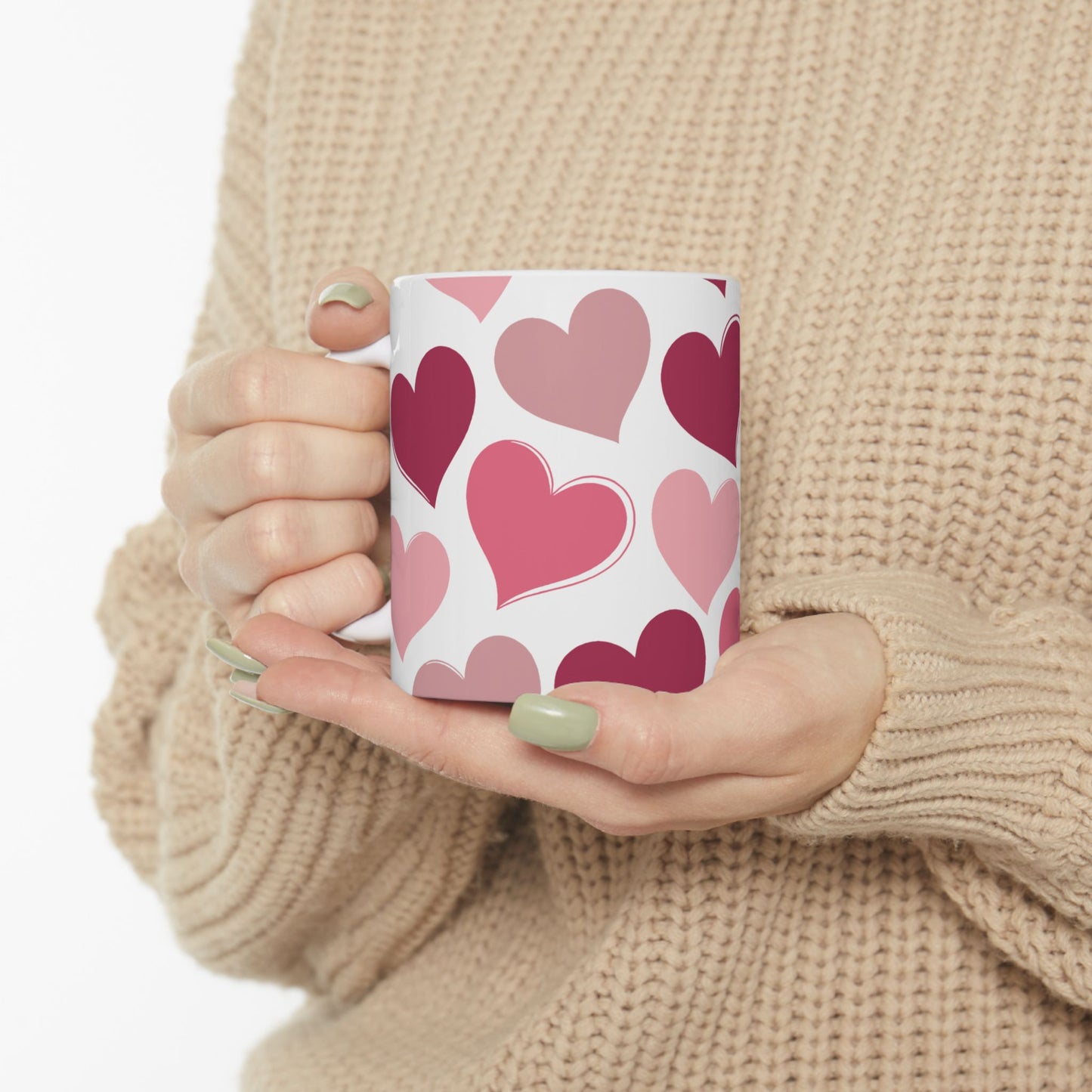 Person holding a mug with pink heart pattern against a beige sweater background