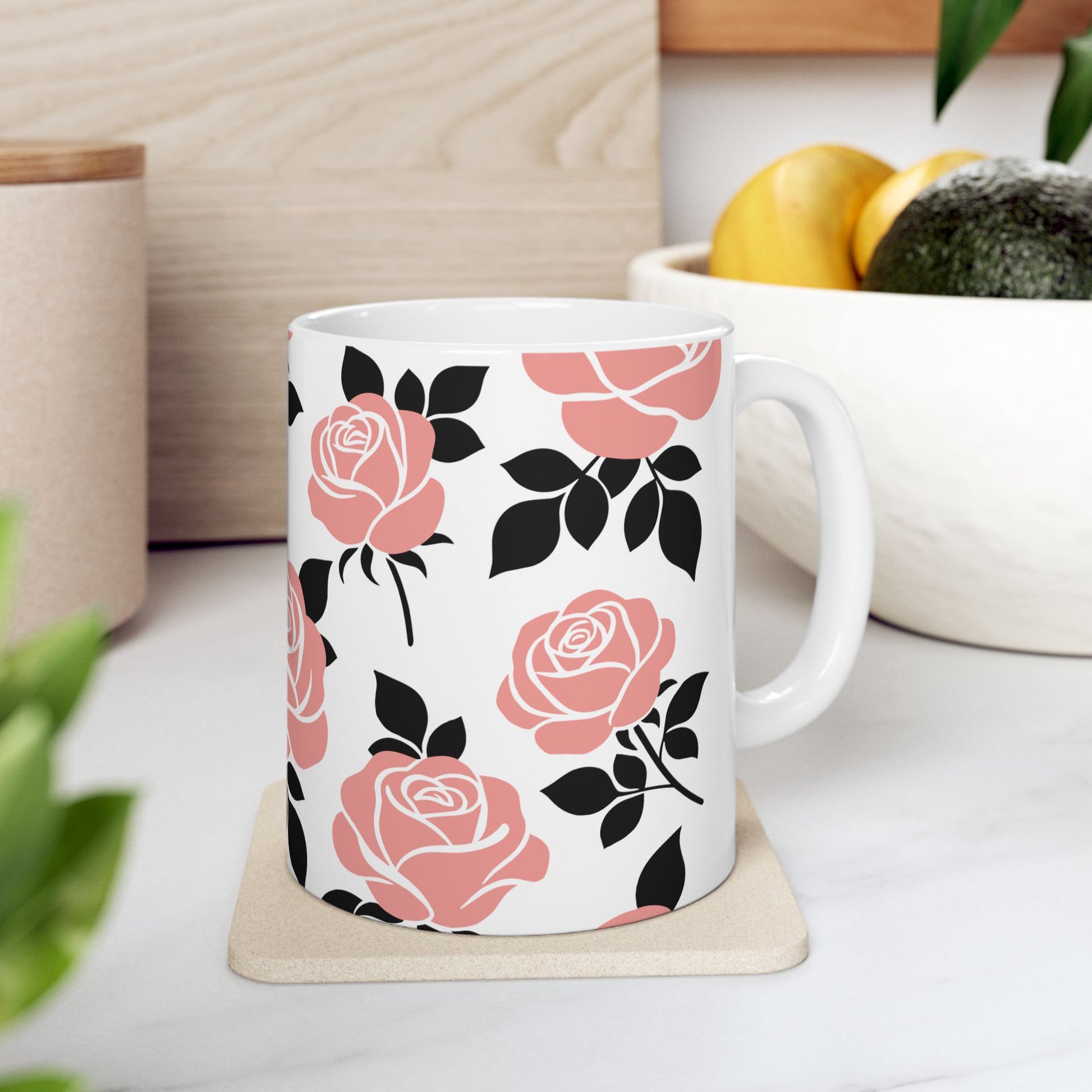 White mug with pink and black floral pattern on a white surface with plants and a bowl in the background