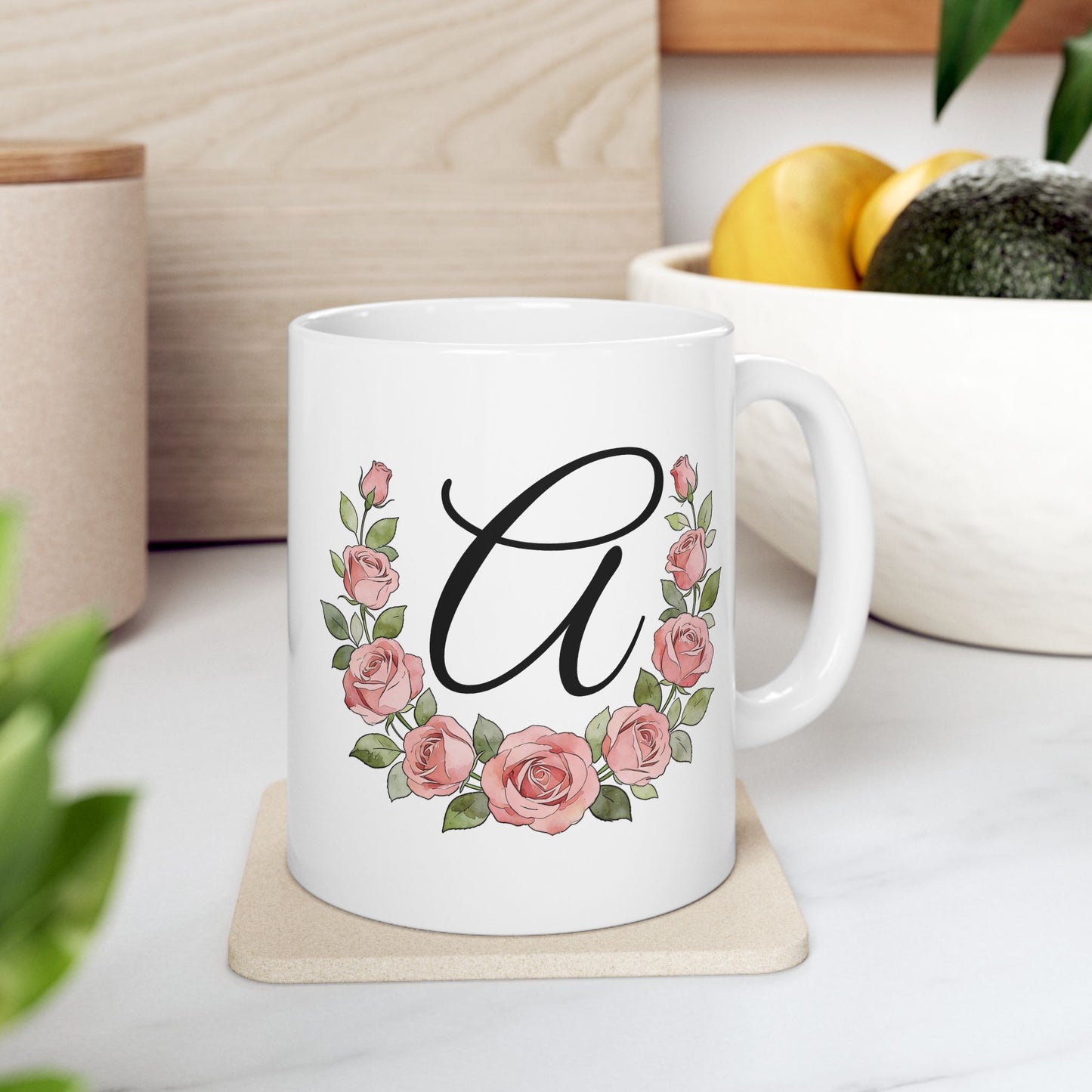 White mug with floral design and letter 'A' on a coaster, surrounded by plants and fruits.