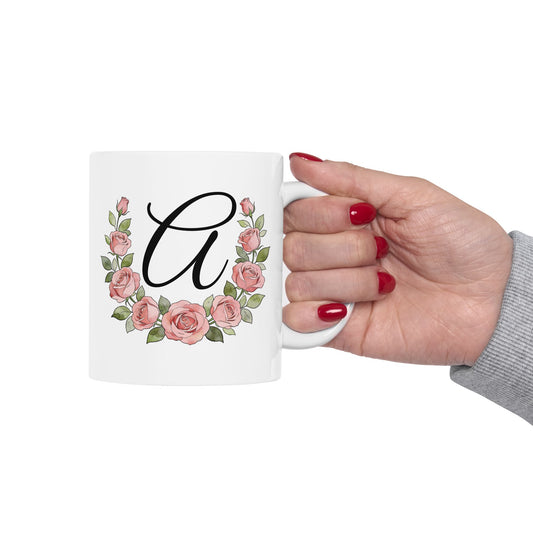 White mug with floral design and letter 'A' held by a hand with red nail polish on a white background